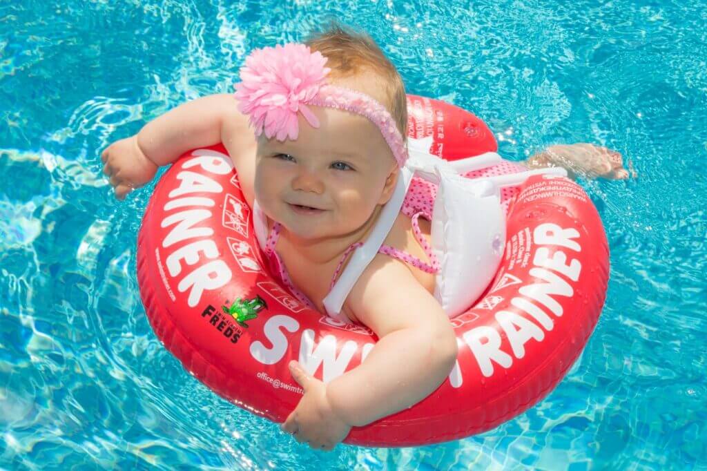 Un bambino sorridente che nuota con un salvagente Swimtrainer rosso.